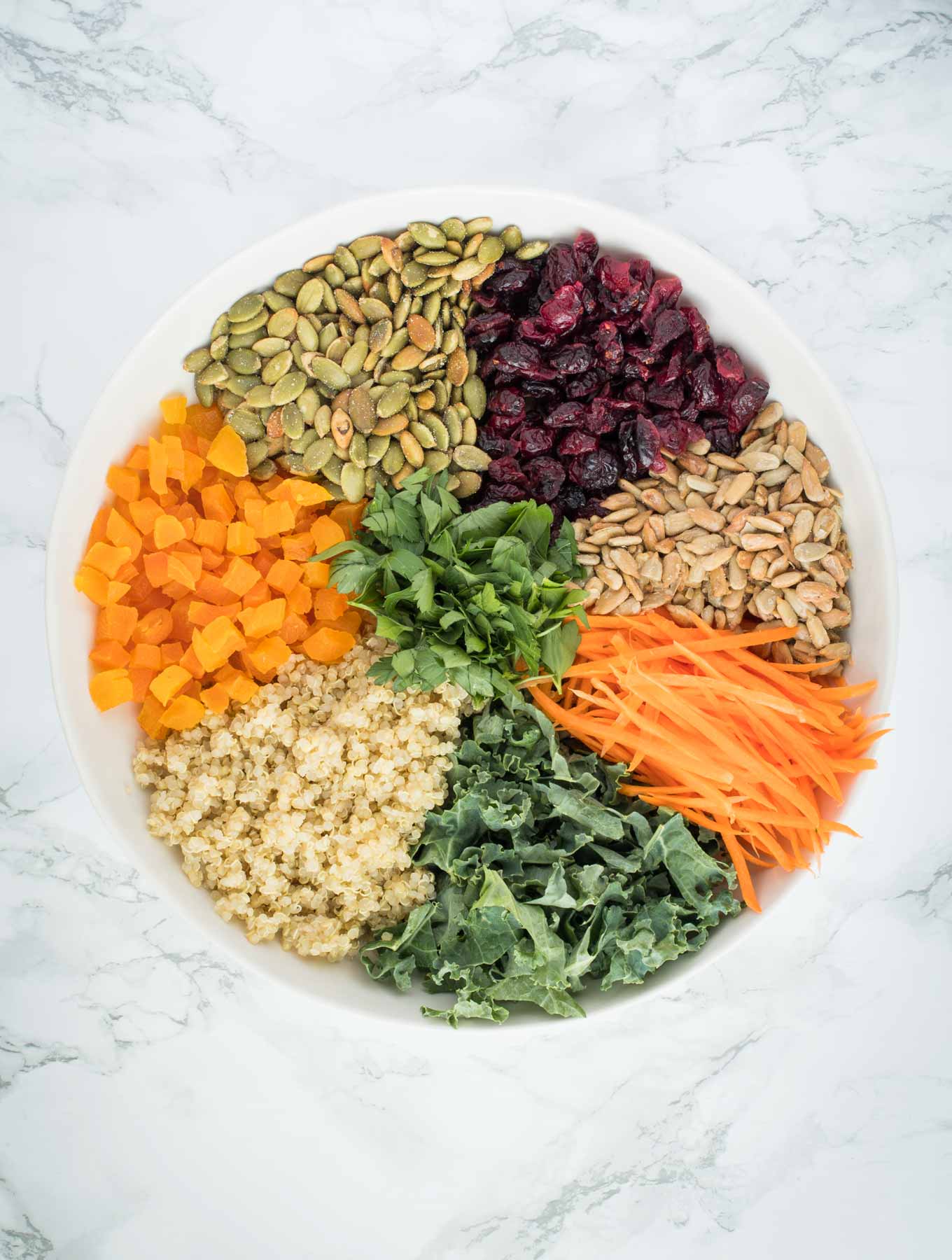 A bowl full of quinoa, dried fruit, seeds, kale, carrots and parsley.