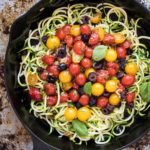 Cast iron skillet of zucchini pasta with tomatoes and olives