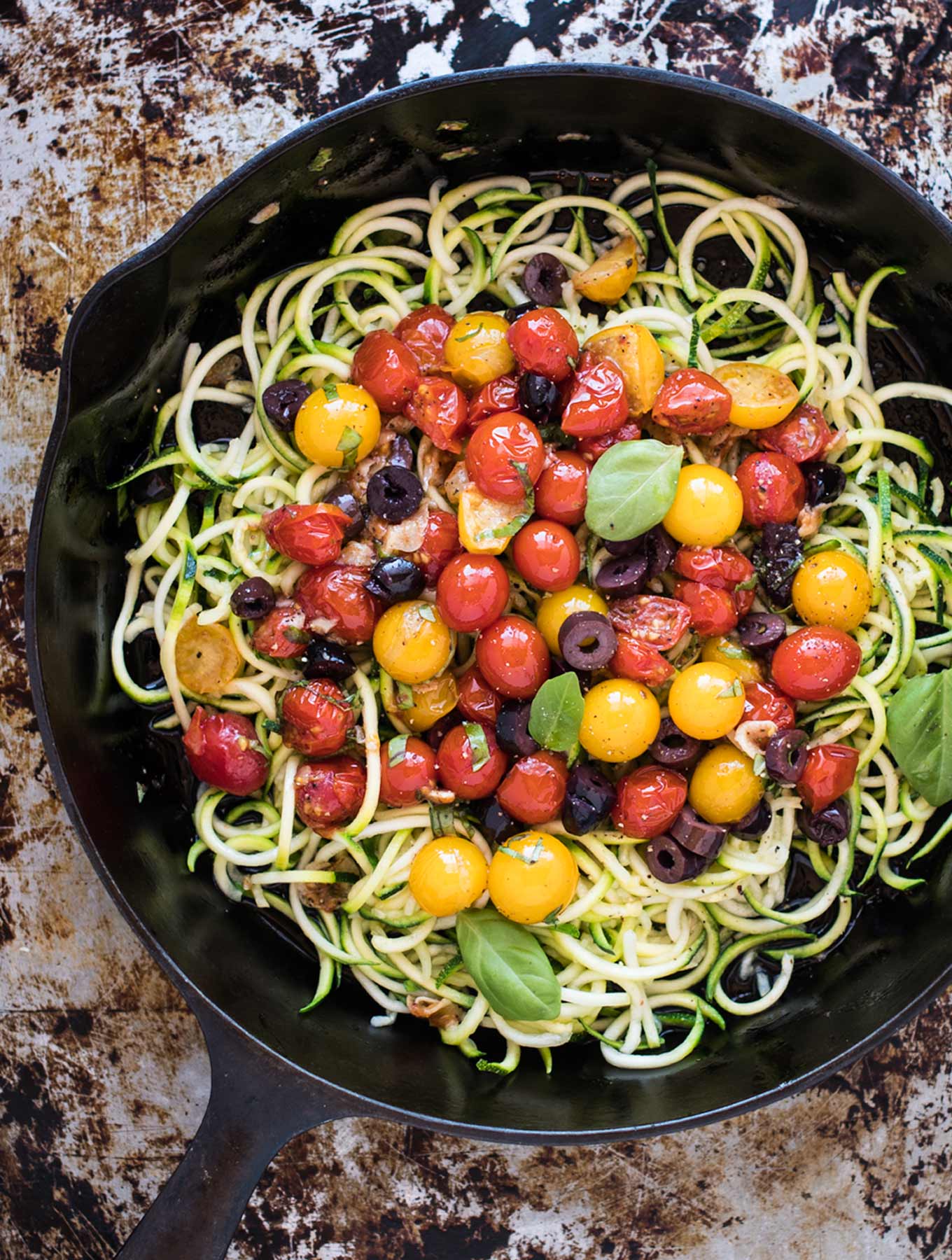 Cast iron skillet of zucchini pasta with tomatoes and olives