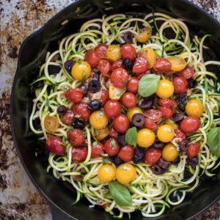 Cast iron skillet of zucchini pasta with tomatoes and olives