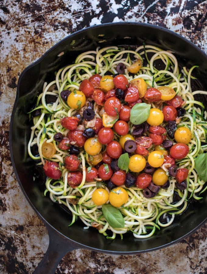 Cast iron skillet of zucchini pasta with tomatoes and olives