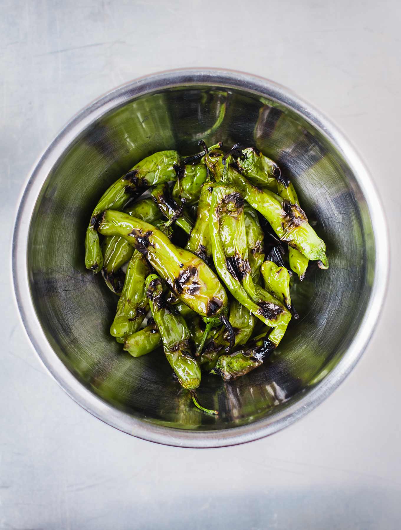 Grilled shishito peppers in stainless bowl