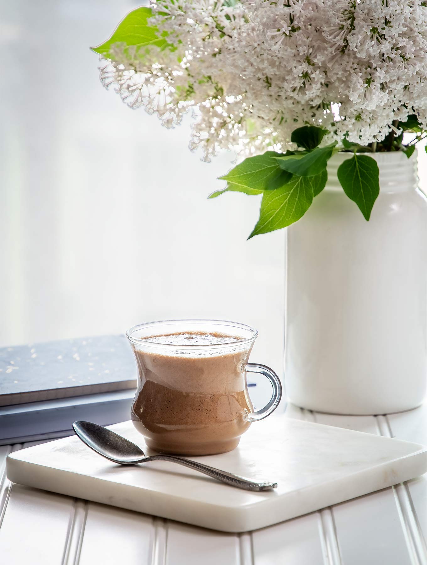 clear mug of cardamom cashew latte on a square marble trivet