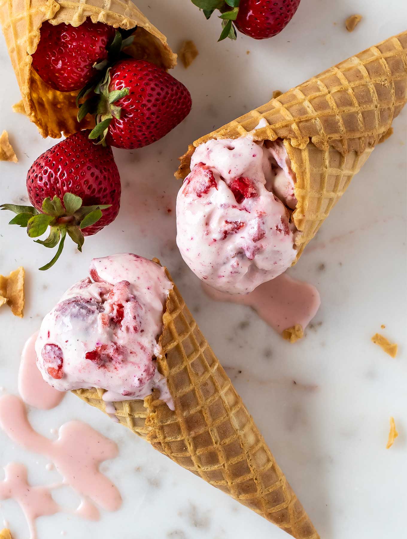 close up of two cones of strawberry rose ice cream on a marble surface