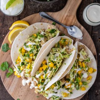 Overhead shot of three fish tacos on a wooden board