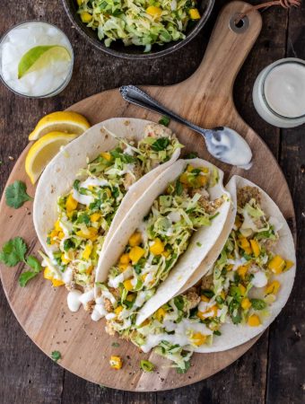 Overhead shot of three fish tacos on a wooden board