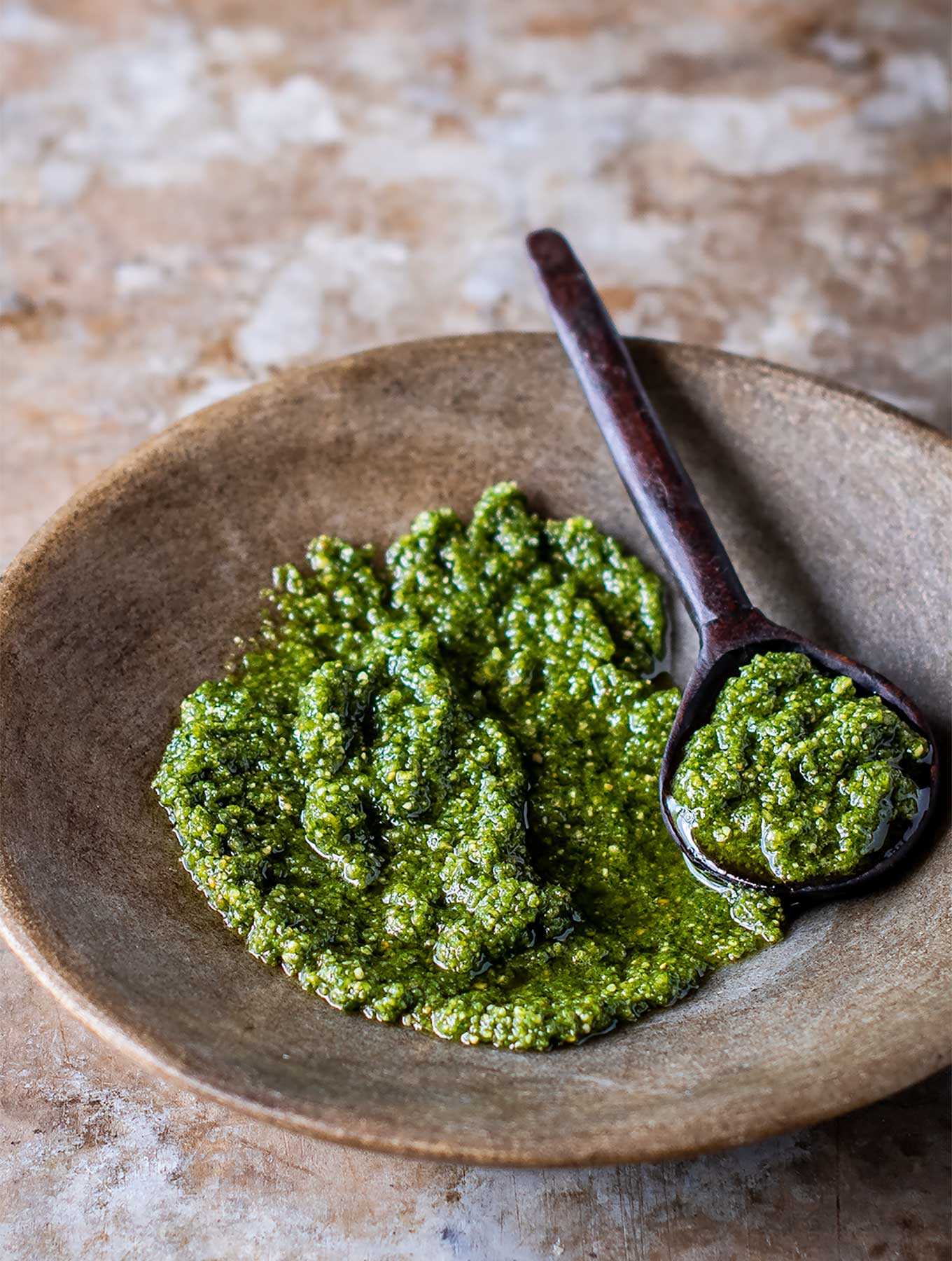 shallow bowl of pumpkin seed pesto with a wooden spoon