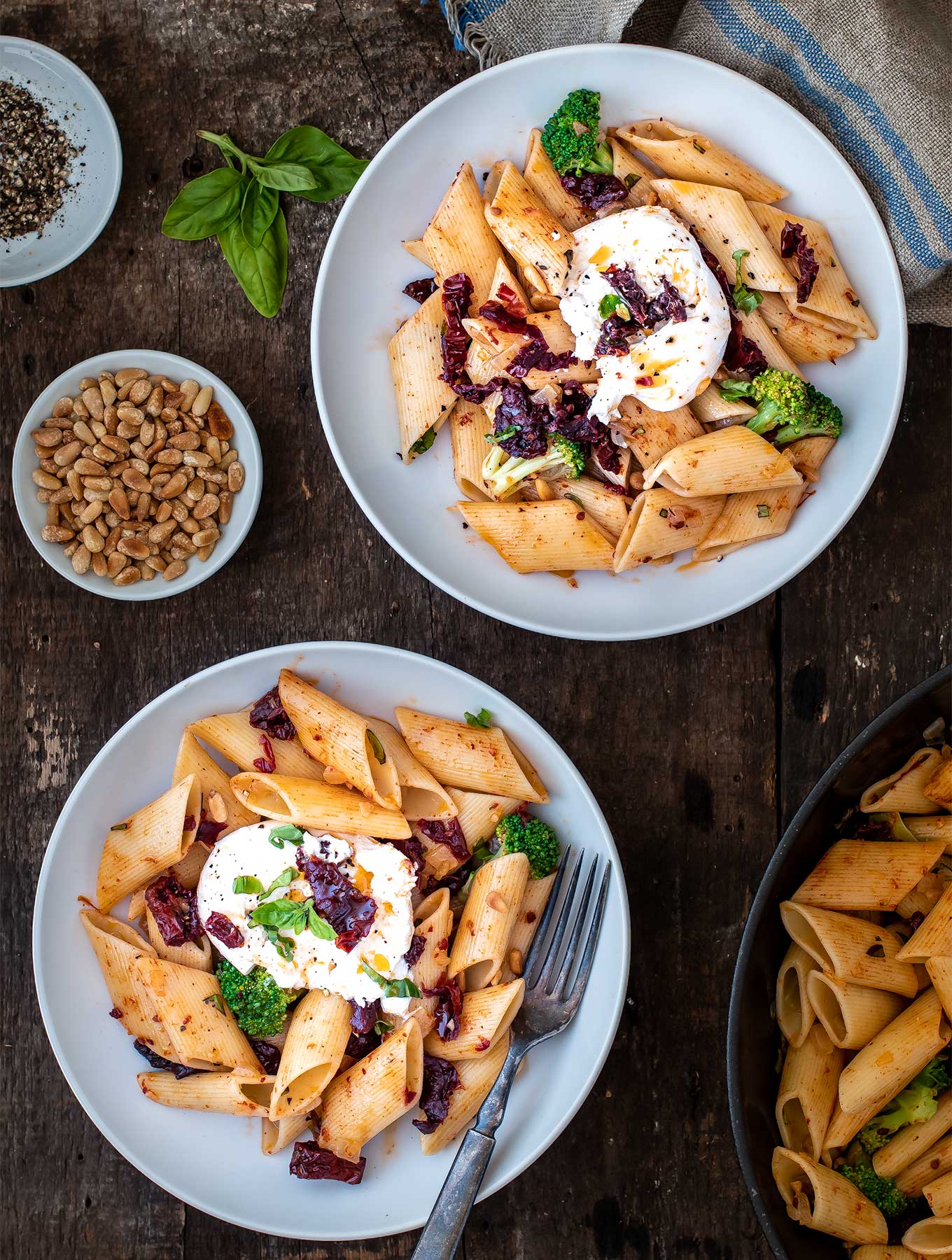 Two bowls of pasta with sun dried tomatoes, broccoli and burrata