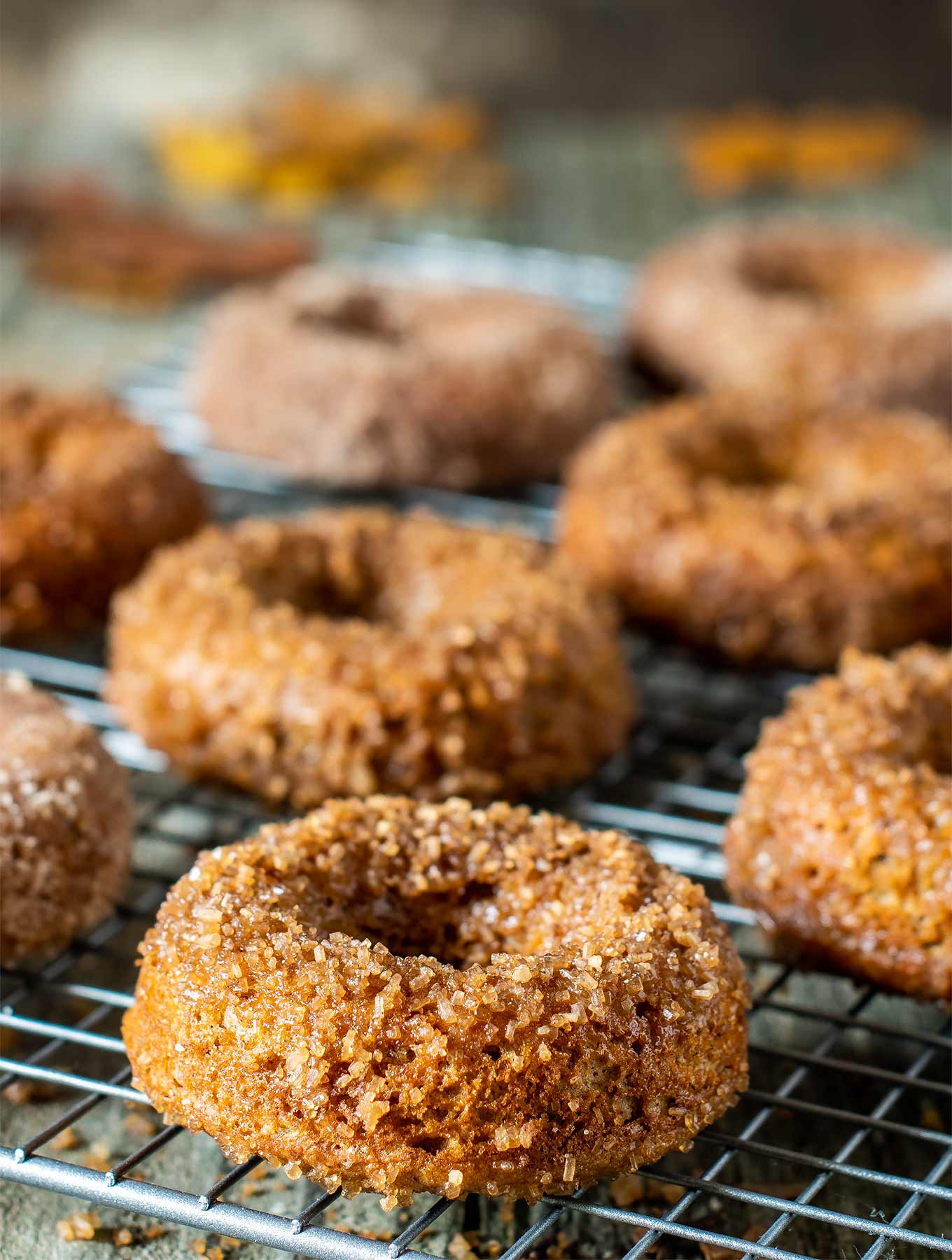 cardamom donuts on a cooling rack with sugar